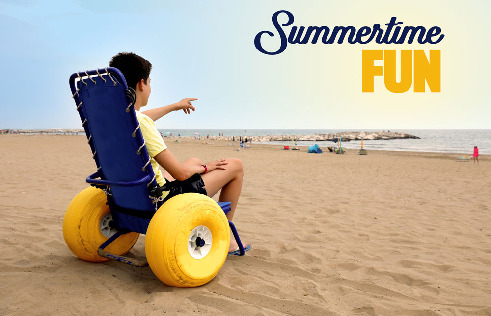 a photo of a boy using a wheelchair on a beach. The wheelchairadapted with large tires for beach travel