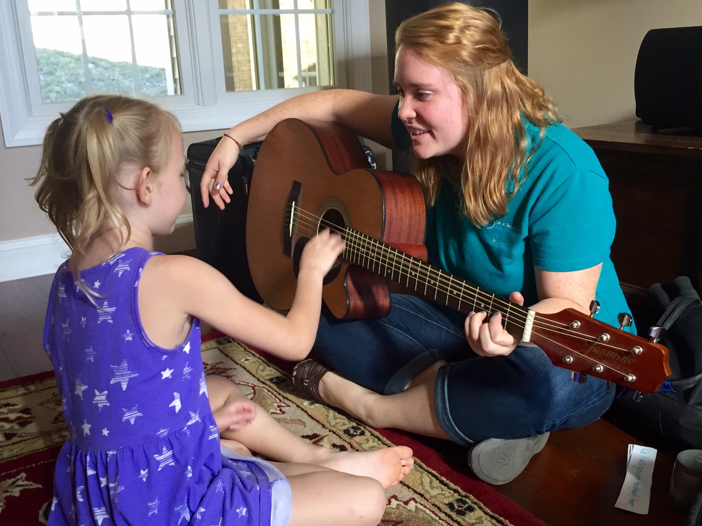 a photo of a young student, age 6, playing a guitar with one of our music therapists