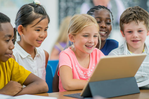 a photo of a group of diverse children gathered around a laptop