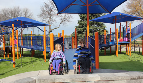 a photo of two children using wheelchairs playing on a accessible playground