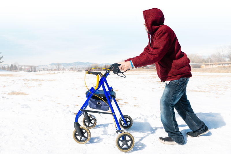 a photograph of a young man using a walker with wheels in the snow