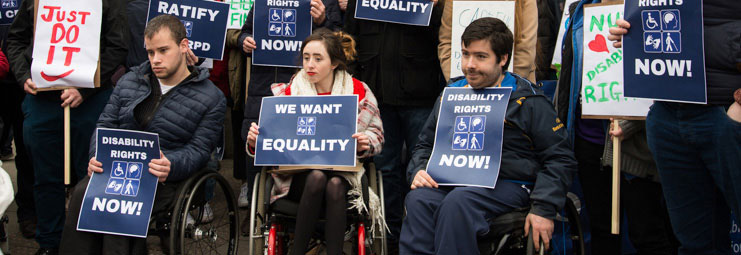 a photo of a protesters in wheelchairs holding up signs that say: Disability Rights Now! and We want equality!
