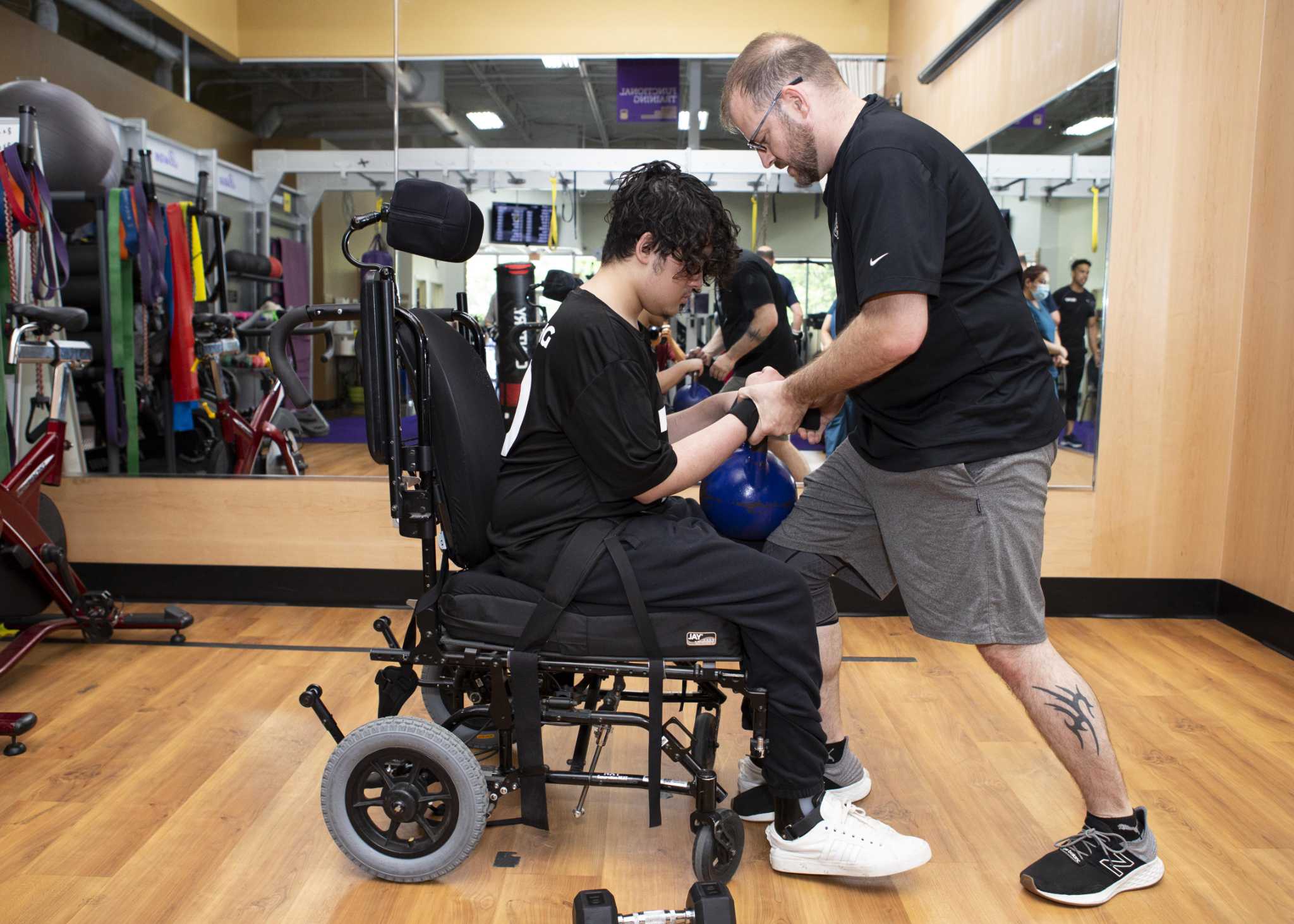 a photo of a man helping another man do core exercises in his wheelchair